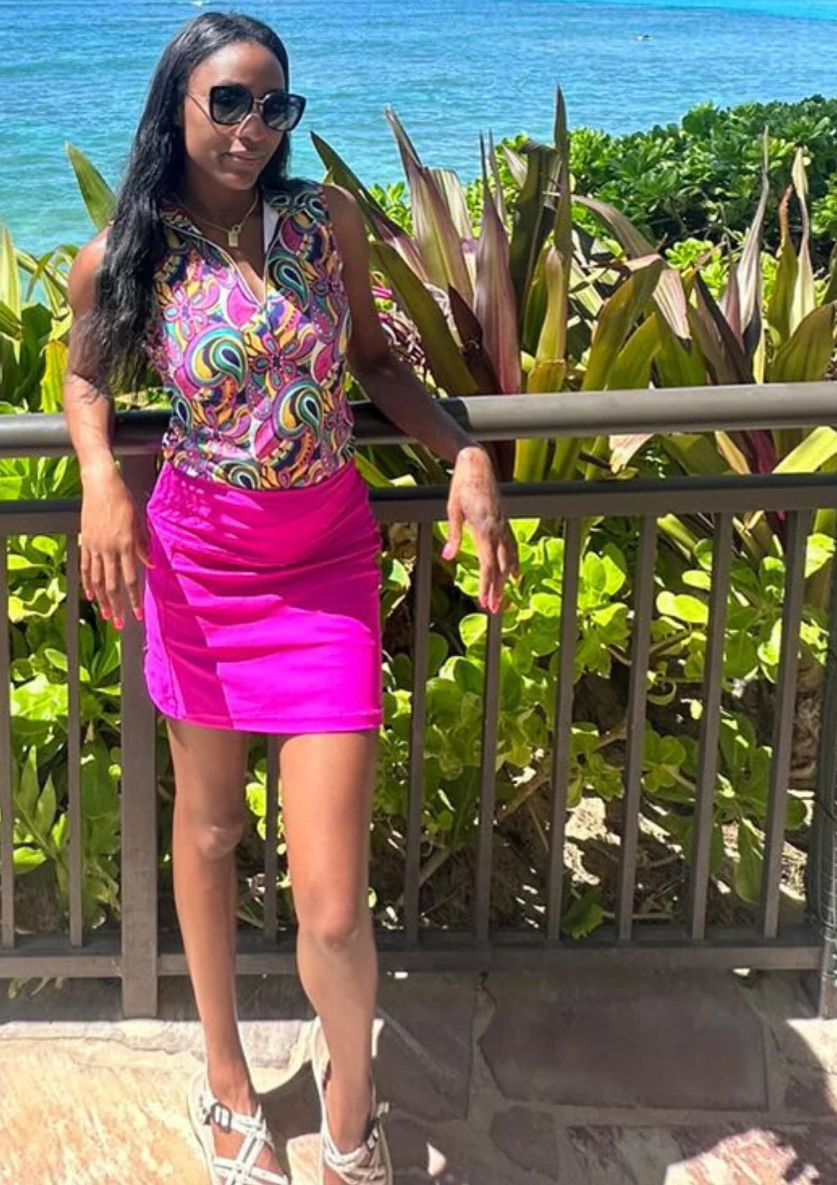 Woman leaning on railing at beach wearing pink skort and paisley top