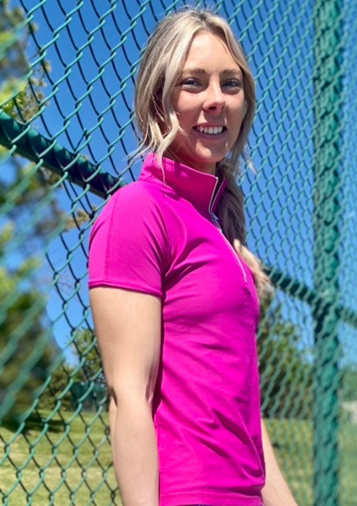 Woman in front of tennis fence wearing Skea designer activewear top in Orchid