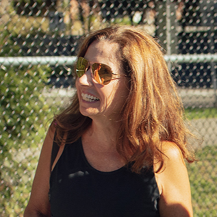 Smiling woman in front of fence wearing Relay aviator sunglasses