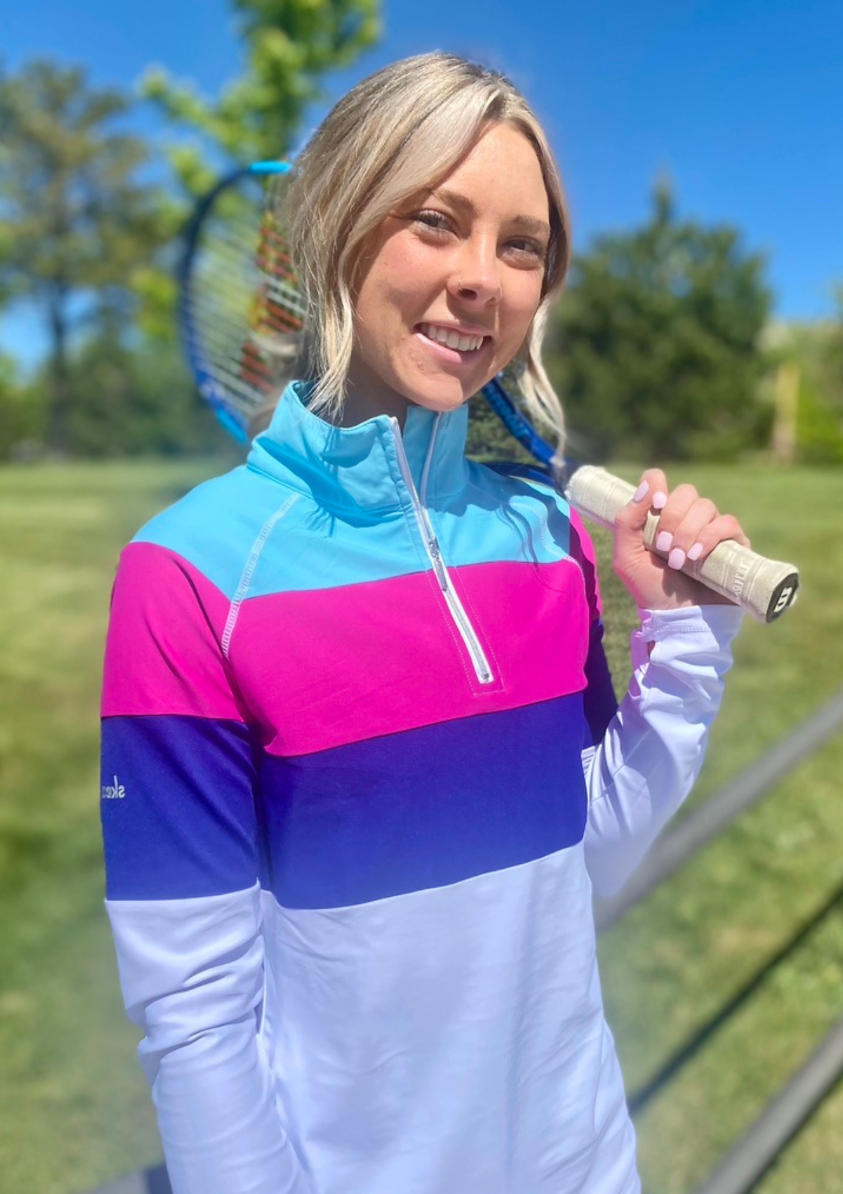 Woman tennis player courtside in woods wearing striped half-zip longsleeve top