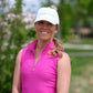 Woman outdoors in trees wearing pink sleeveless zip top and white baseball cap
