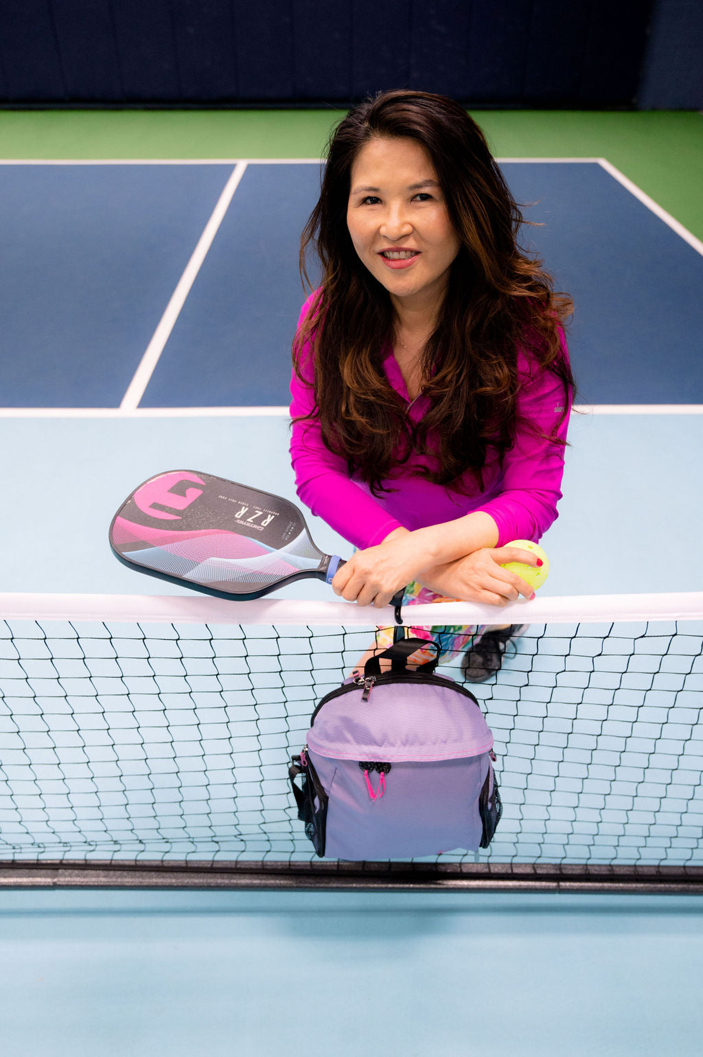 Woman on court wearing 1/4 zip pink top and holding women's designer pickleball tote