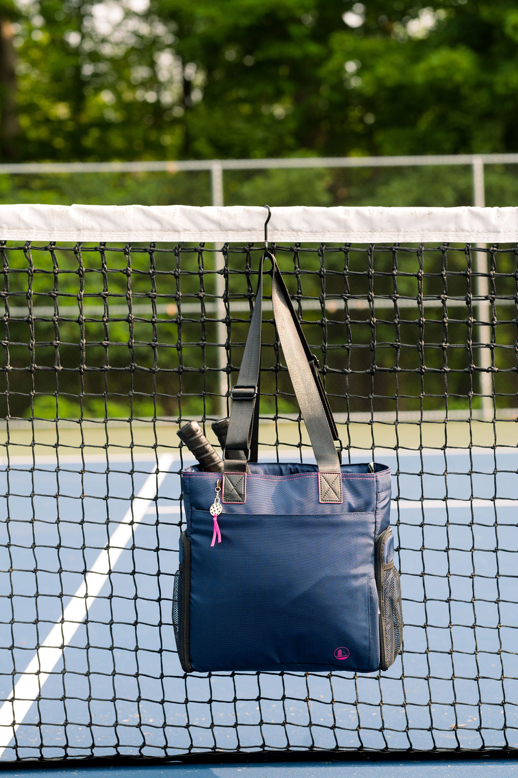 Elegant navy pickleball tote hanging on net, equipped with fence/net hook to keep your back accessible and off the ground