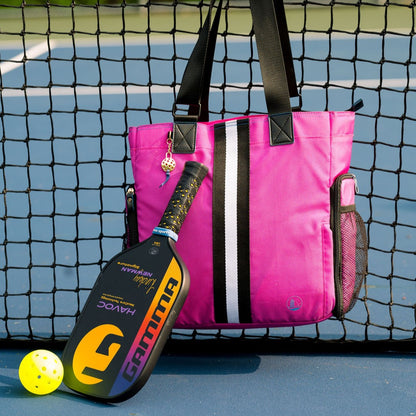Women’s designer Pickleball Tote in Pink w/Black/White Vertical Stripe hanging from net, with Gamma paddle and ball propped in front