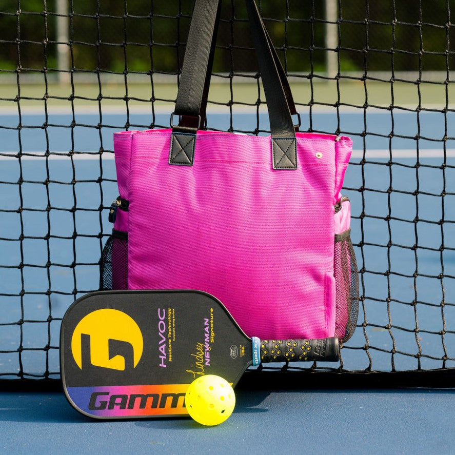 Women’s designer Pickleball Tote in Pink hanging from net, with Gamma paddle and ball propped in front