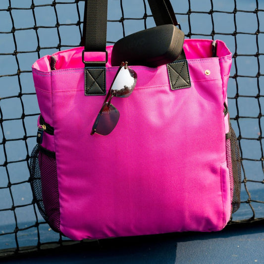 Pink Gasparilla Pickleball and Tennis Tote hanging on net on the court with Revo Descend Rimless Sunglasses and case hanging from tote