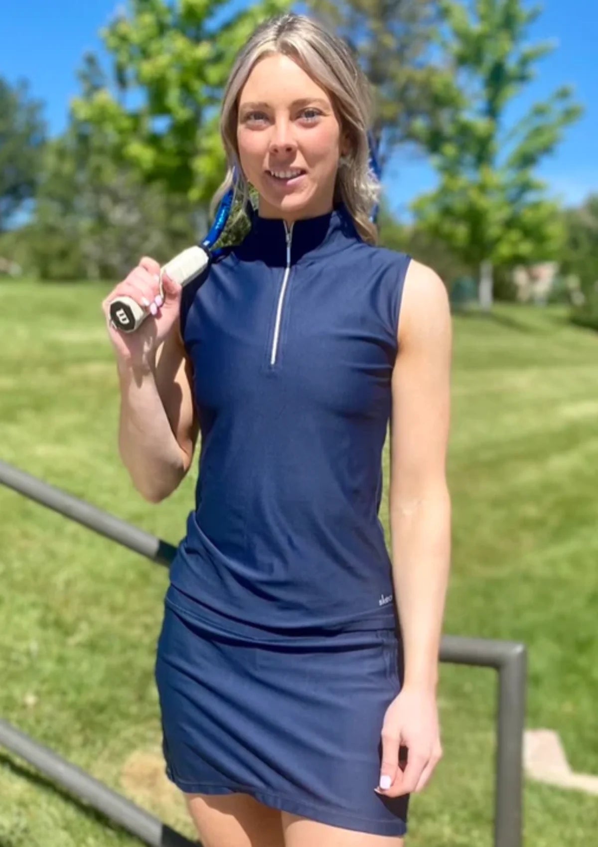 Woman outdoors with tennis racket wearing navy skort and half-zip top