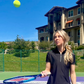 Woman bouncing tennis ball on court in front of mountainside home