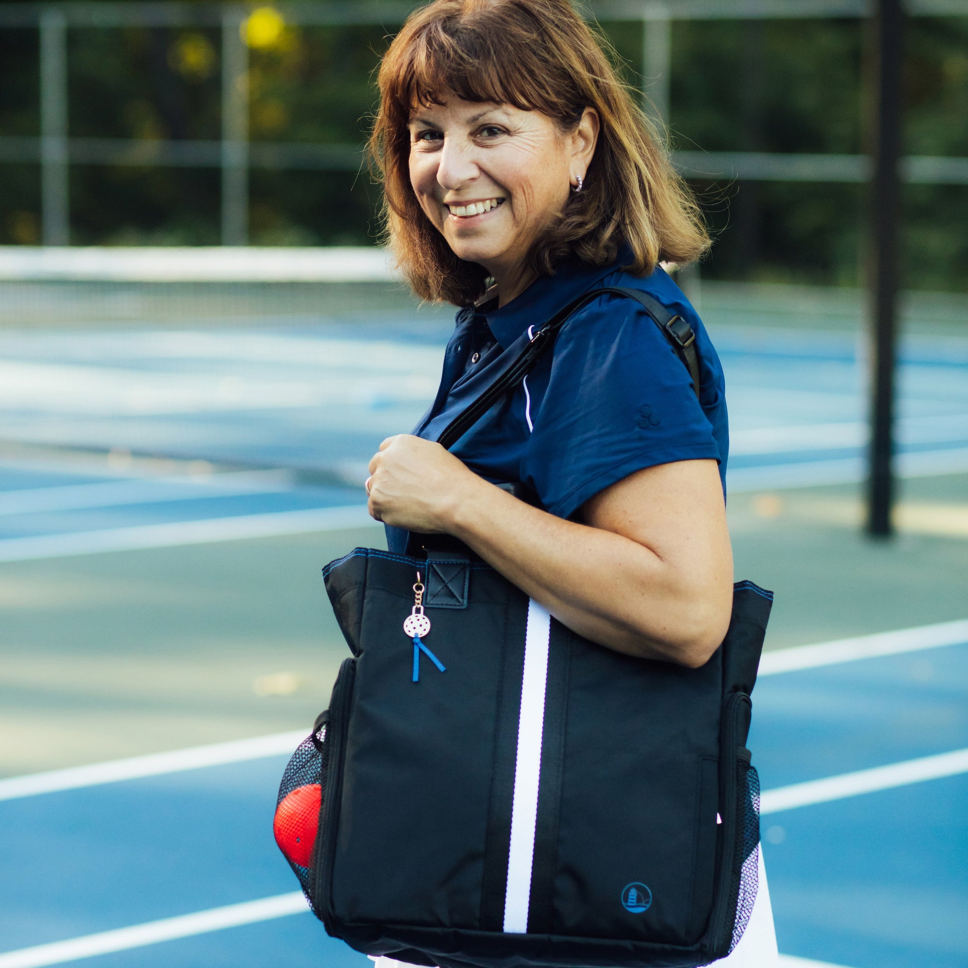 Smiling Woman on court with designer pickleball tote in black with black/white mesh strip on her shoulder – Lighthouse Sports
