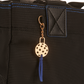 Detail on women’s designer pickleball tote - cast metal pickleball charm, gold tone with Blue suede tassel
