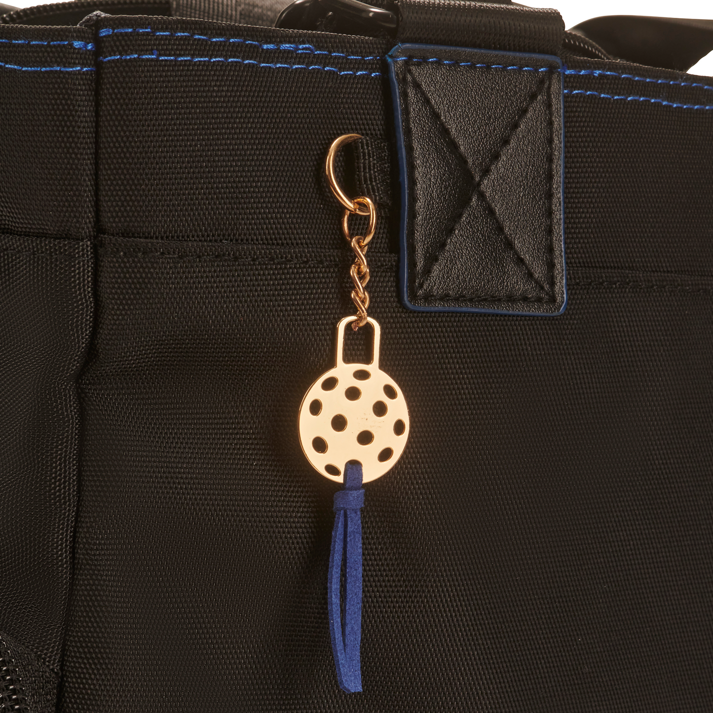 Detail on women’s designer pickleball tote - cast metal pickleball charm, gold tone with Blue suede tassel